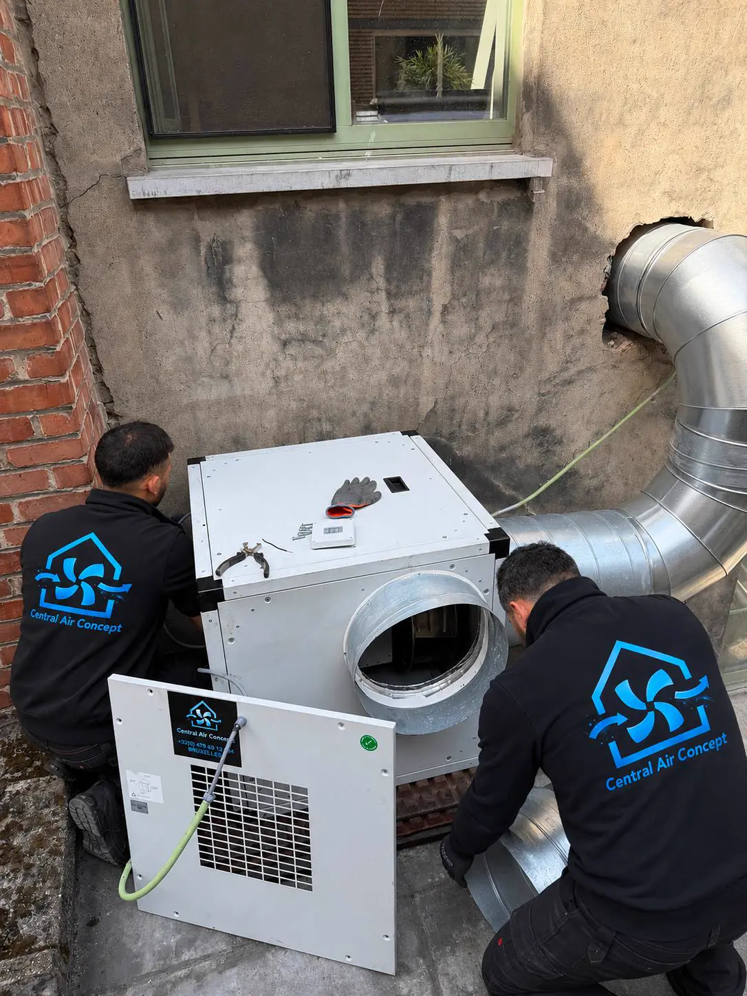 Deux techniciens Central Air Concept installent un caisson d'extraction raccordé aux conduits spiralés sur un chantier à Bruxelles
